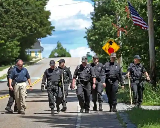 State Police walk down the street after searching through the woods for evidence after a woman visiting her mother was found slain